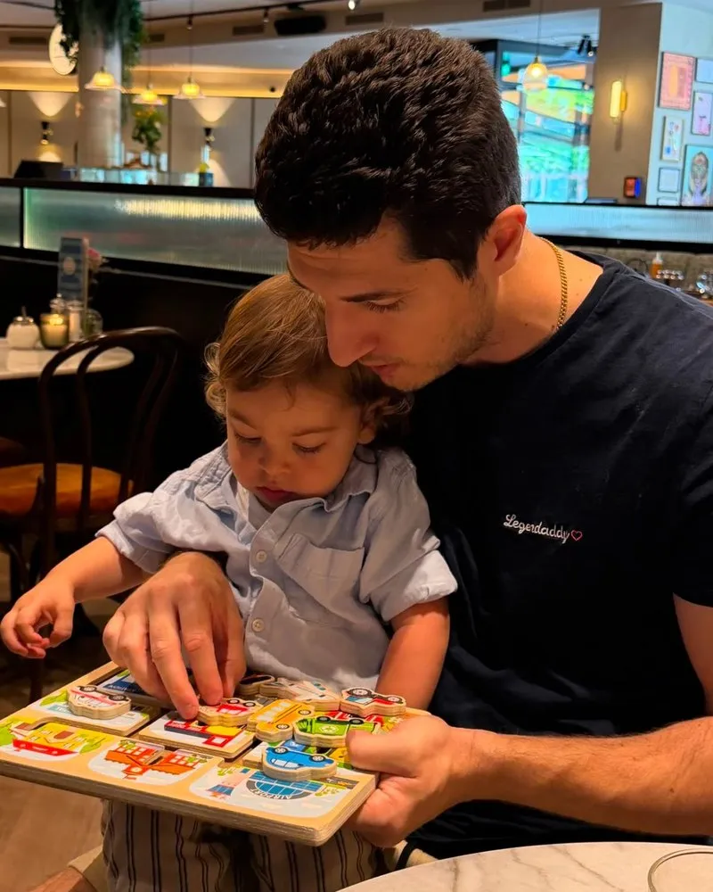 Asim with his young son on his lap, fitting the pieces of a wooden puzzle together.